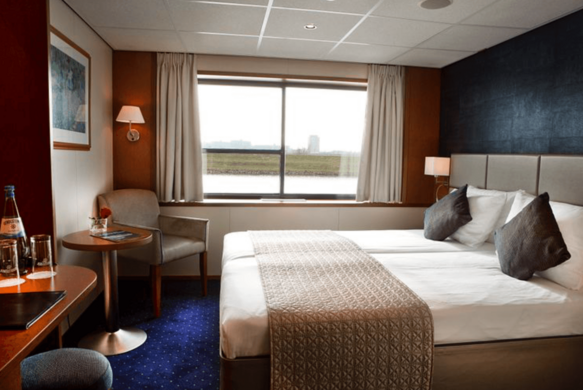 Kreuzfahrtkabine mit Doppelbett, Schreibtisch und Fenster mit Blick aufs Meer.